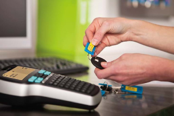 Drukarka DYMO LM 420P podpięta przez kabel USB do komputera, naklejana etykieta z 2 wierszami tekstu na breloczek do kluczy